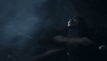 a woman is standing in the dark with her arms outstretched and looking up .