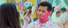 a man with pink paint on his face is standing next to a woman in a crowd .