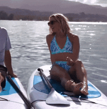 a woman in a bikini is sitting on a paddle board