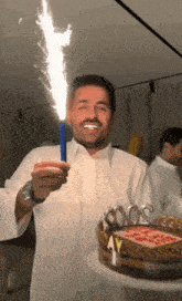 a man in a white shirt is holding a sparkler in front of a birthday cake