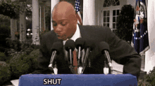 a man in a suit and tie is standing behind a podium that says shut on it