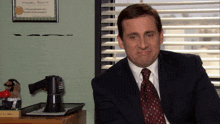 a man in a suit and tie is sitting in front of a sign that says michael scott on it