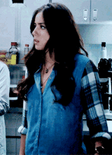 a woman wearing a plaid shirt and a blue shirt is standing in a kitchen