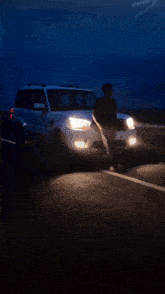 a man stands in front of a car with the headlights on