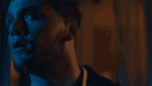 a close up of a man 's face in a dark room with blue light behind him .