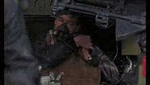 a man in a leather jacket is sitting in a vehicle with a gun