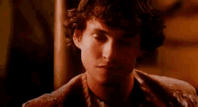 a close up of a man 's face with curly hair and a brown jacket .