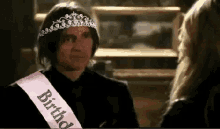a man wearing a tiara and a pink sash with the word birthday on it .
