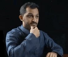 a man in a blue shirt is pointing at his watch while wearing a watch .