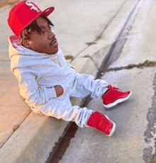 a man wearing a red hat and red shoes is sitting on a curb .