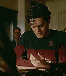 a man in a red and black sweater is sitting at a table holding a book in his hands .