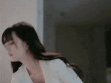 a woman in a white shirt is standing in a room with her eyes closed and her hair blowing in the wind .