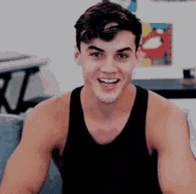 a young man wearing a black tank top is smiling and sitting on a couch .