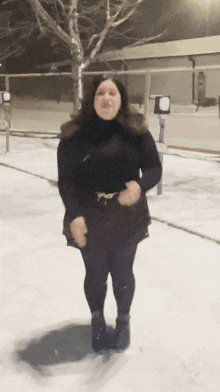 a woman in a black dress stands in the snow