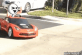 a red car with a smiley face on it is driving down a street .