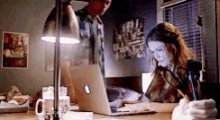 a man and a woman are sitting at a desk looking at a laptop computer .