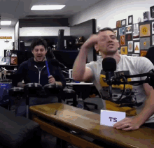 two men are playing drums in front of a microphone and a sign that says ts