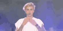 justin bieber is wearing a white shirt and a microphone on stage .