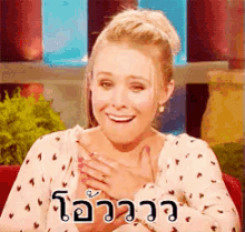 a woman in a polka dot shirt is smiling and holding her hands to her chest in a foreign language .