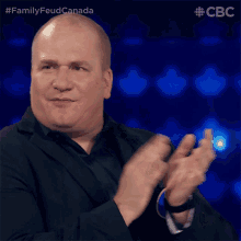 a bald man in a suit is clapping his hands in front of a blue background with the letters cbc on it