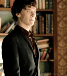 a man in a suit stands in front of a bookshelf with the words smarthly on the bottom right