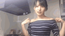 a woman wearing a striped off the shoulder top is standing in a kitchen .