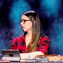 a woman wearing glasses and a plaid shirt is sitting at a table with a tablet and the word really written on the table