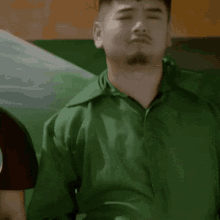 a man in a green shirt is making a face with his eyes closed