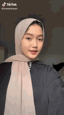 a girl wearing a hijab and a black shirt has a tiktok watermark on her face