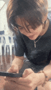a young man wearing a black shirt and a necklace is playing a game on his phone