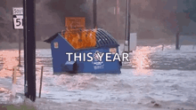 a blue dumpster is on fire in a flooded area with the words this year written above it