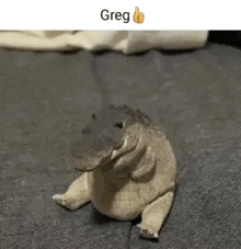 a stuffed alligator is sitting on the floor with a thumbs up .