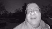 a man wearing glasses and a scarf is smiling in a black and white photo