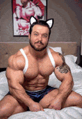a man wearing cat ears sits on a bed in front of a picture of a man