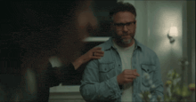 a man wearing glasses and a denim shirt is being helped by a woman