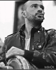 a man with a beard is wearing a leather jacket and playing a drum .