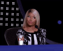 a woman is sitting in front of a microphone holding a cup that says ok .