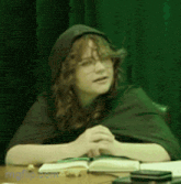 a woman wearing a cape is sitting at a table with a book