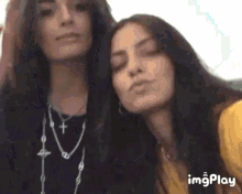 two women are posing for a picture with their eyes closed . one of the women is wearing a cross necklace .