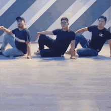 three men are sitting on the floor with one wearing a black champion shirt