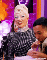 a woman in a black and white polka dot dress is sitting next to a man drinking from a cup .