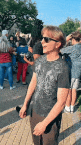 a man wearing sunglasses and a black shirt with a skull on it stands in front of a crowd of people