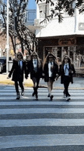 four women in suits and ties cross a street in front of a building that says ' boutique avenida ' on it