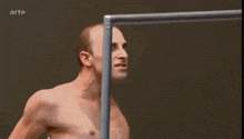 a shirtless man is standing next to a metal pole with arte written on the bottom right corner