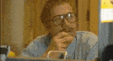 a man with glasses and a mustache is sitting at a counter in a bank .