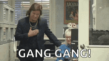 a man in a suit is standing next to a woman in an office and says gang gang !