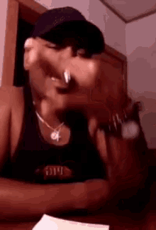 a man wearing a hat and a tank top is sitting at a table with his hands in his pockets .