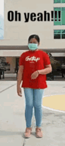 a girl wearing a mask and a red shirt is standing in front of a building with the words oh yeah written on it .