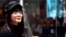 a woman wearing glasses and a hat is standing in front of a window