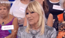 a woman is sitting in a crowd of people with a name tag that says viperissima on it .